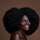 Studio portrait of a smiling Black woman with natural Afro hairstyle.